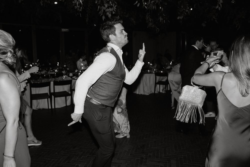 Black and white photo of wedding guests dancing energetically on a dark dance floor.