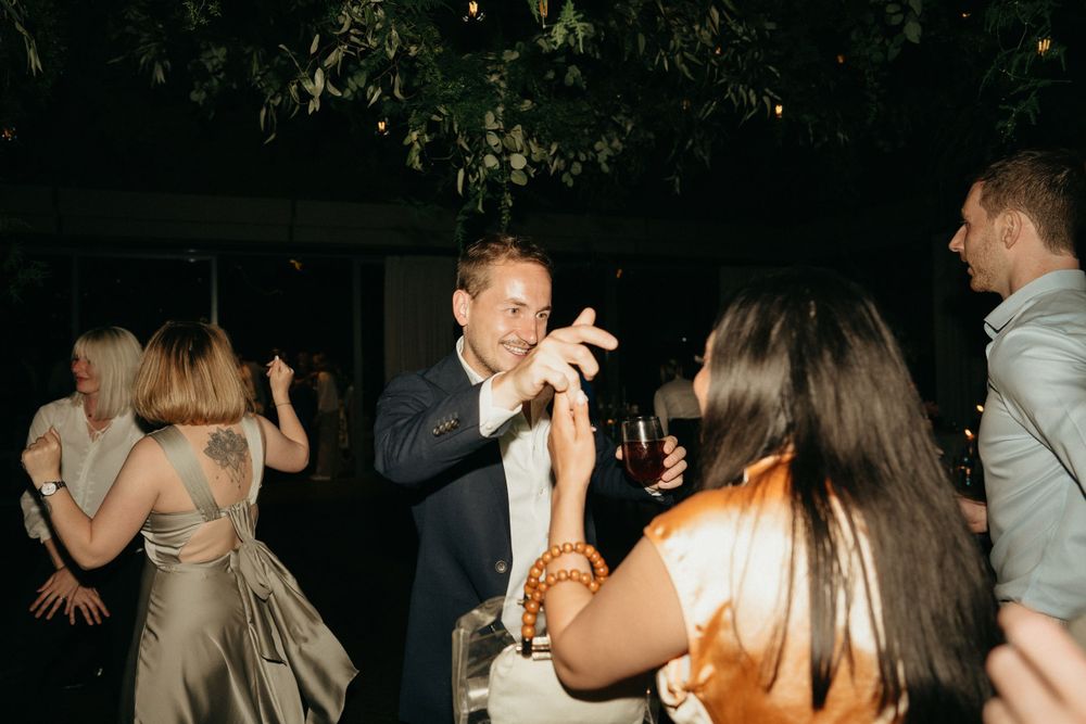 Wedding reception guests dancing and celebrating with enthusiasm under outdoor lighting.