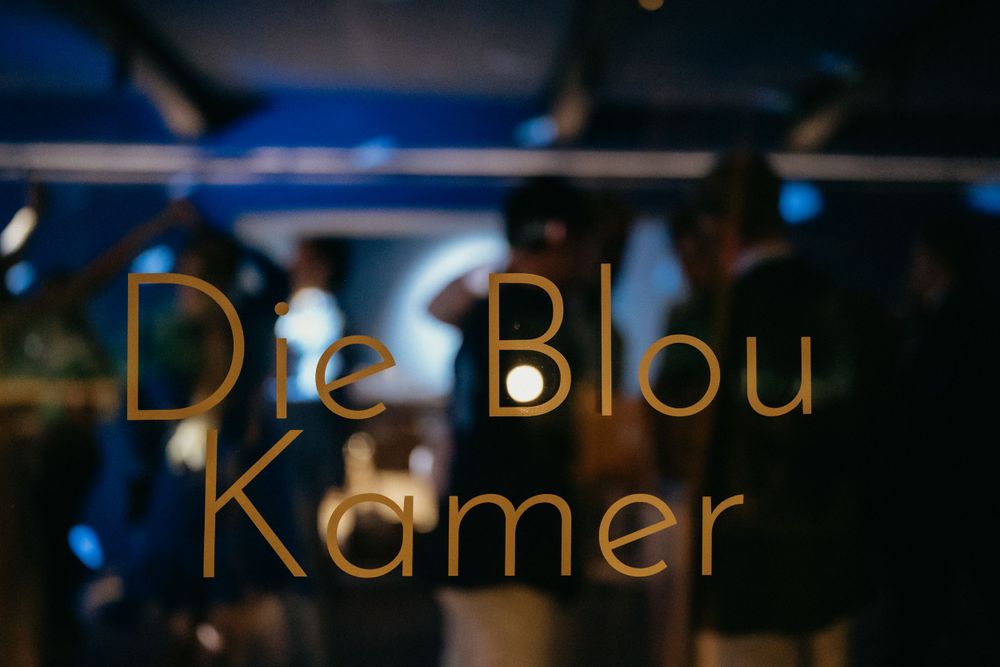 Illuminated gold text reading 'De Blou Kamer' against a dark blue background with bokeh lights.
