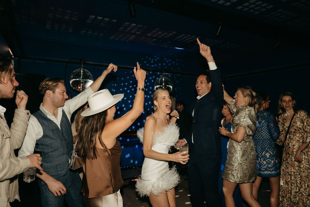 Crowded dance floor at wedding reception with celebrants raising hands in joyful dancing.