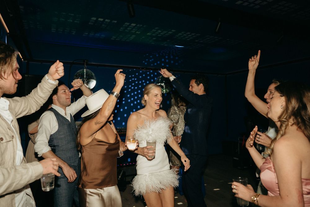 Wedding party dancing and celebrating on a dark dance floor with hands raised in excitement.