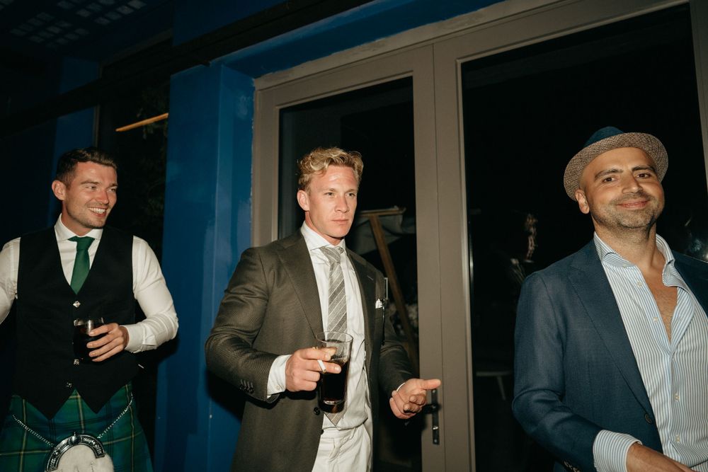 Three men in formal attire enjoying drinks and conversation at an evening party.