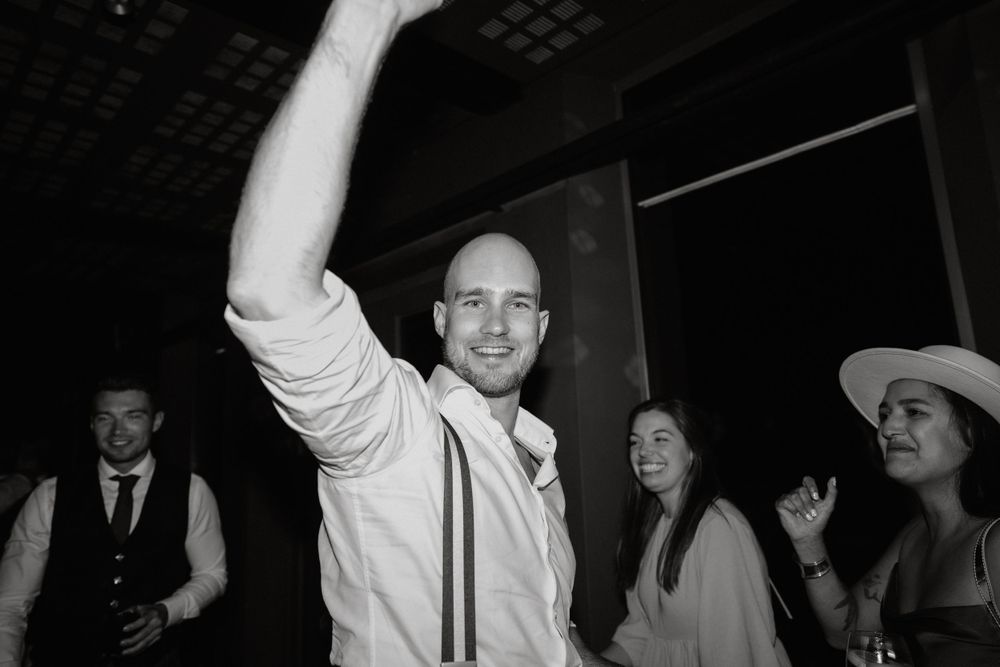 Guest celebrating with raised arm during wedding reception party in black and white photography.