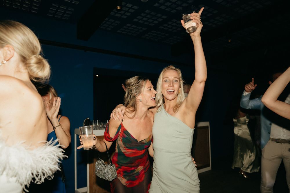 Wedding reception guests dancing and celebrating with drinks on the dance floor.
