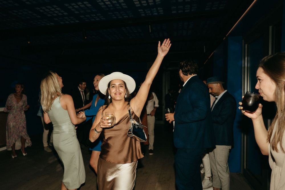 Party guests dance and celebrate on a dark dance floor with one wearing a white cowboy hat.