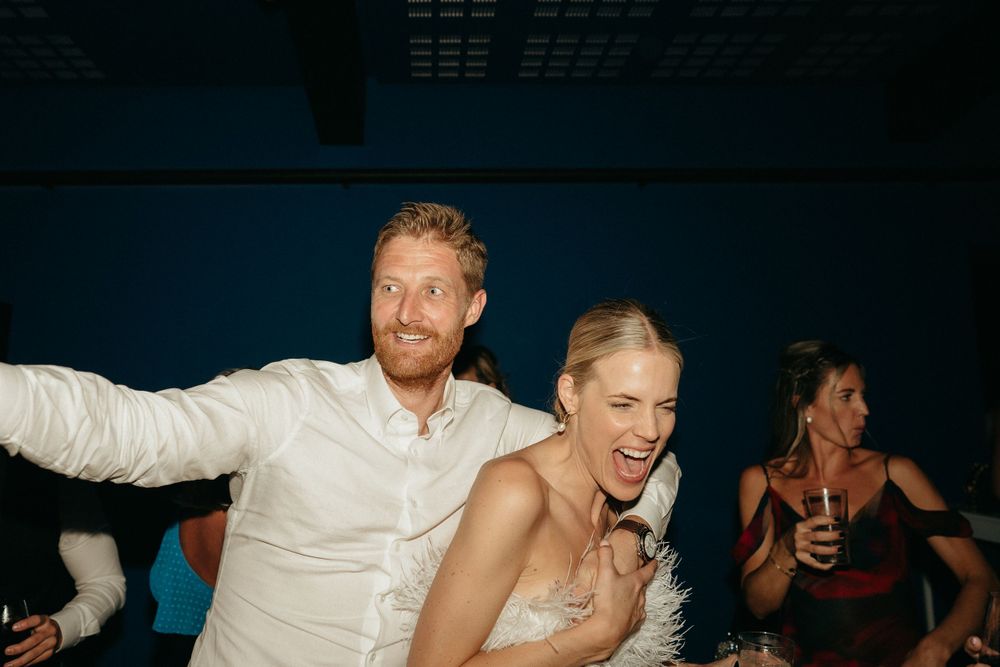 Wedding guests dance enthusiastically during a celebration in a dimly lit venue.