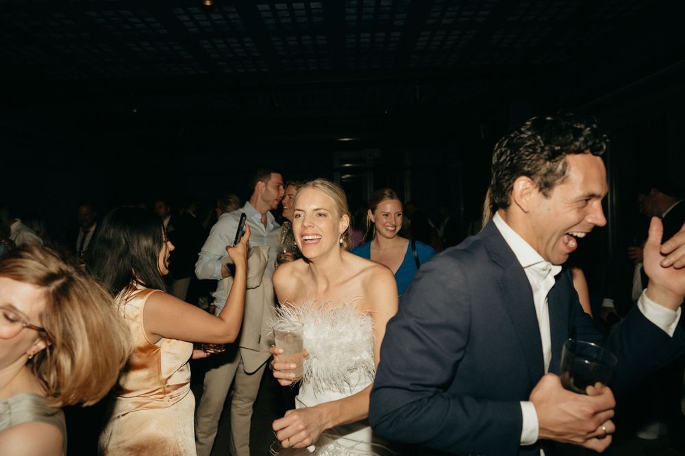 Wedding guests dancing and celebrating at an evening reception under dim lighting.