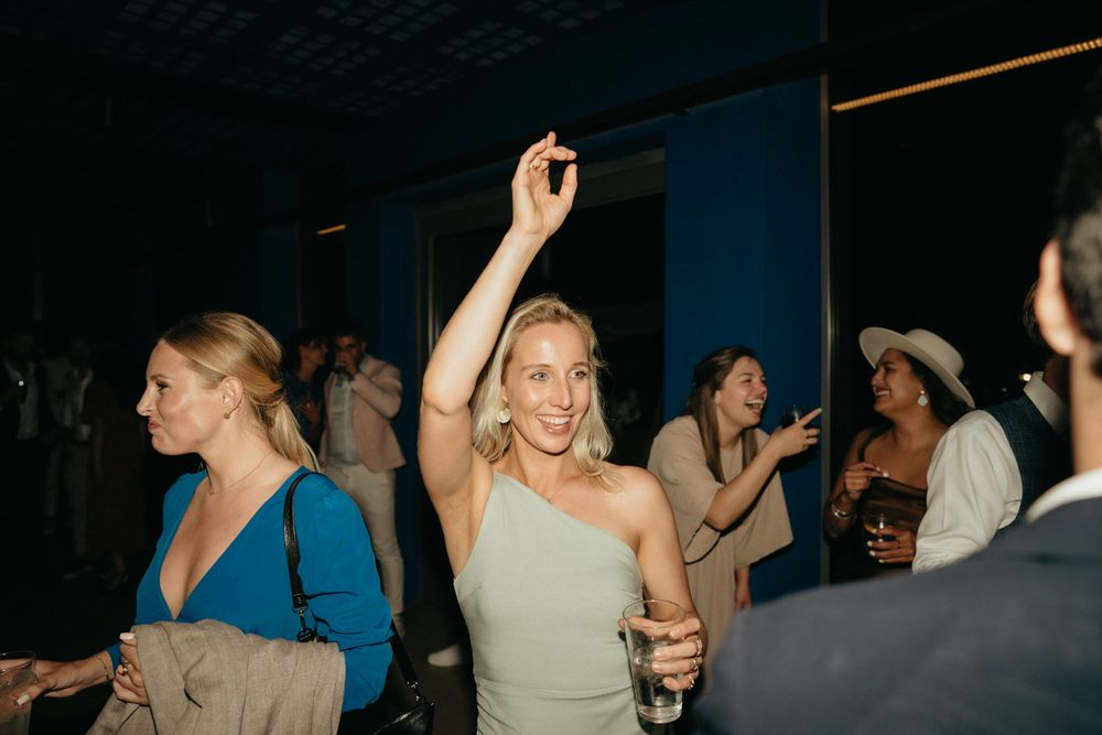 Energetic party guests dancing and raising their hands while enjoying drinks at a nighttime celebration.