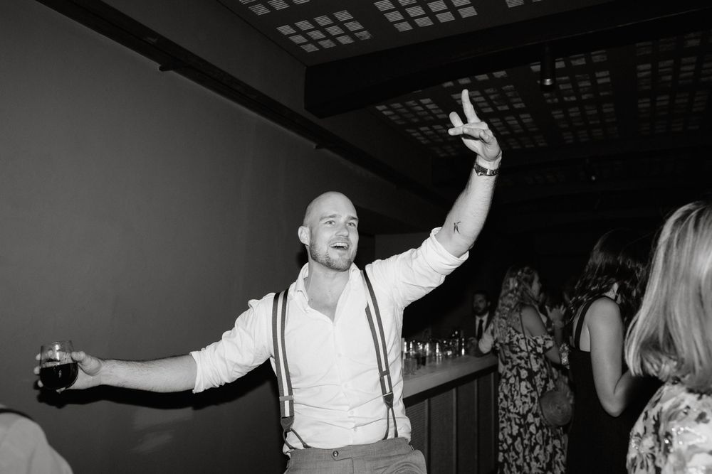 A guest in suspenders dances enthusiastically at a dimly lit wedding reception.