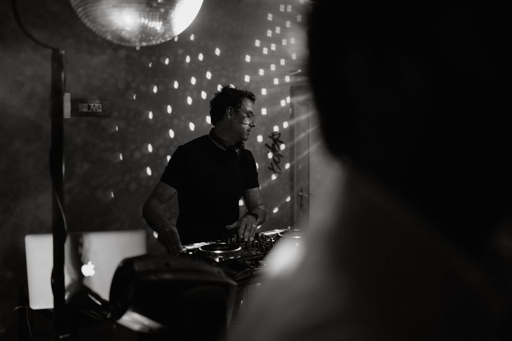 A silhouetted DJ performs under a disco ball with twinkling lights creating a moody atmosphere.