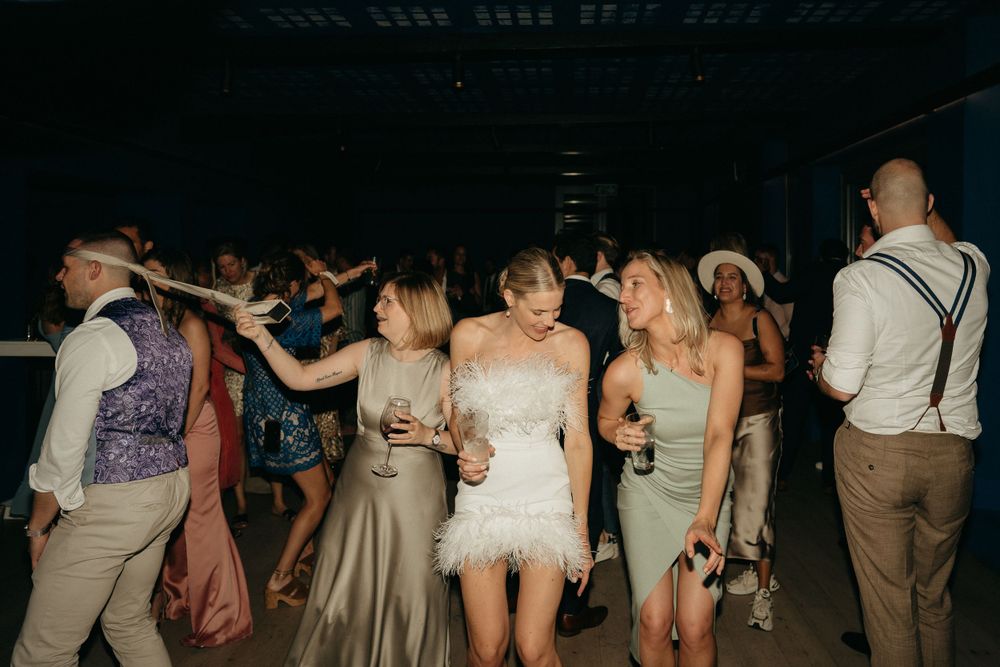Wedding guests dance and celebrate on a dimly lit dance floor at a reception.