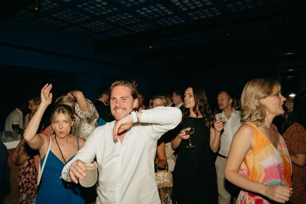 Wedding guests dance joyfully on a dark dance floor at the reception.