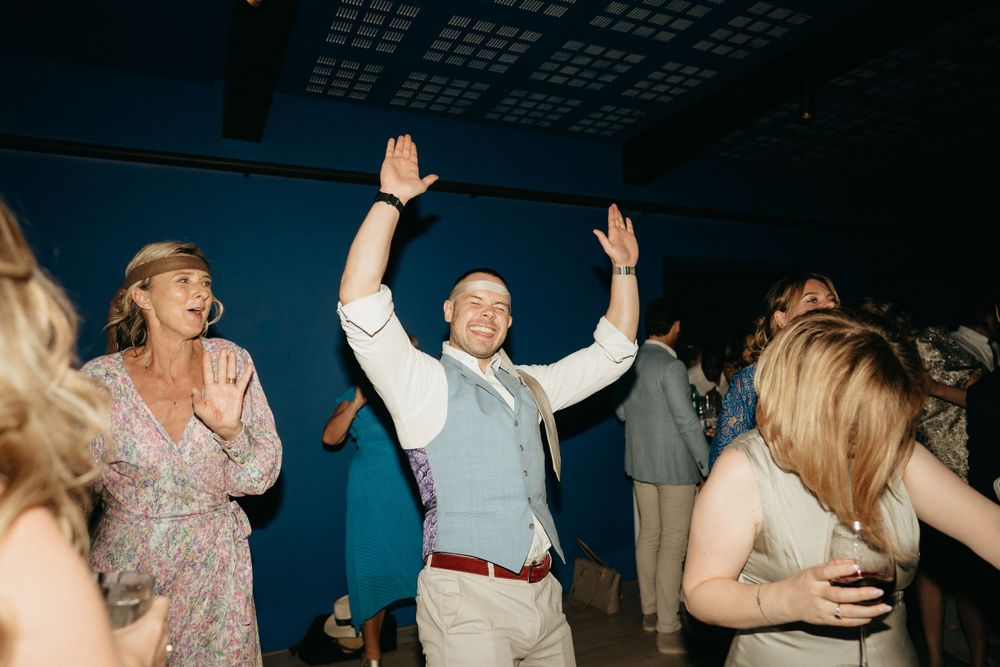 Wedding guests dance joyfully on a dark blue-lit dance floor during an energetic reception celebration.