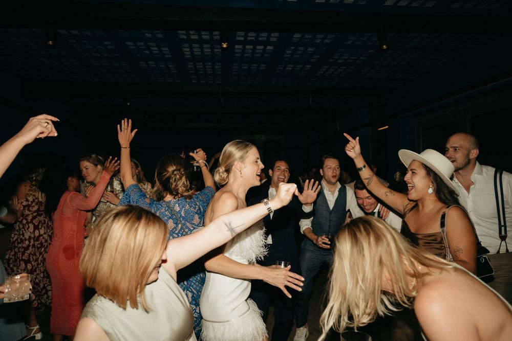 Energetic wedding guests dancing with hands raised during celebration on crowded dance floor.