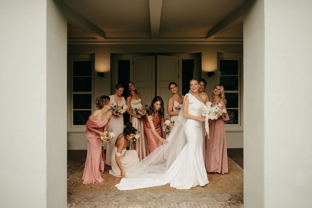 Wedding party gathered in hallway helping with final dress adjustments before ceremony.