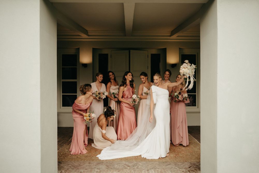 A wedding party poses together in a covered walkway with pink bridesmaid dresses.