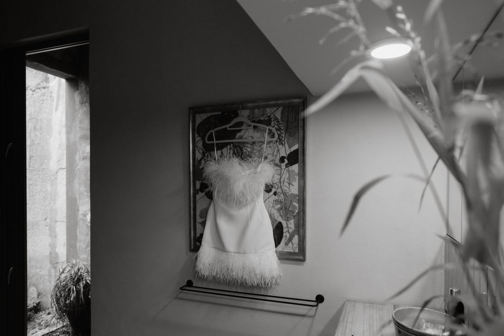 A black and white photograph showing a wedding dress displayed on a wall next to a window.