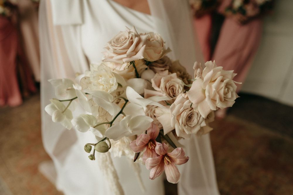Elegant wedding bouquet featuring pale pink and white roses with delicate greenery against white fabric.