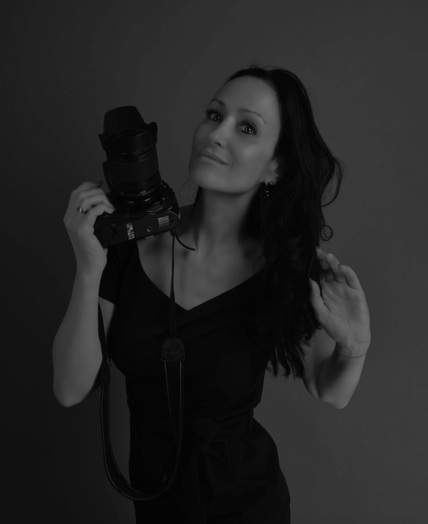Black and white portrait of photographer holding camera while posing in studio.