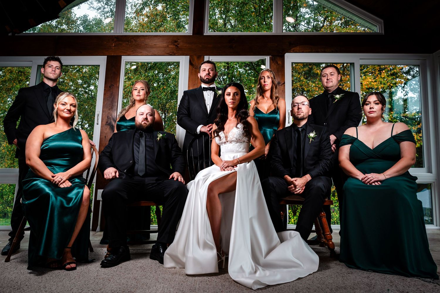 Formal wedding party portrait with bridesmaids in dark dresses and groomsmen in tuxedos.
