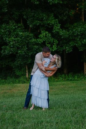 A couple dances and dips in a sunlit meadow surrounded by lush greenery.
