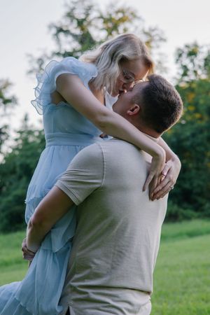 A romantic couple embraces while standing in a sunny outdoor field.