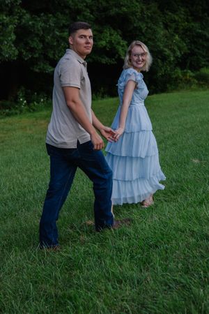 A playful couple walks through a grassy field during golden hour.