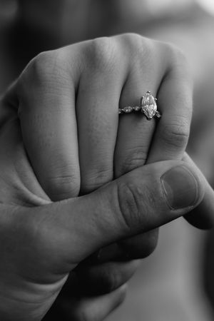 Black and white close-up of hands displaying an engagement ring.