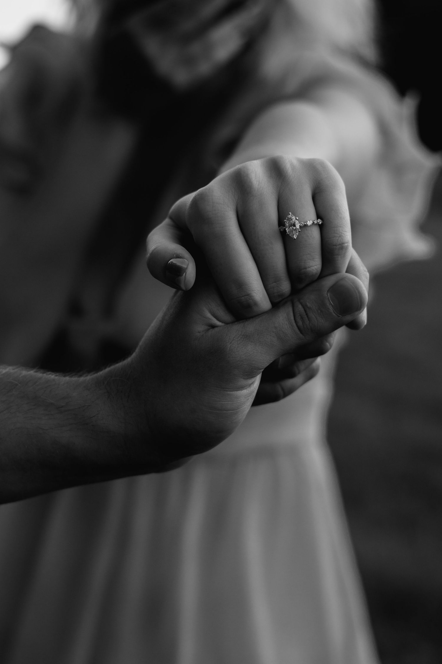 Dramatic black and white shot of hands with an engagement ring against a dark background.