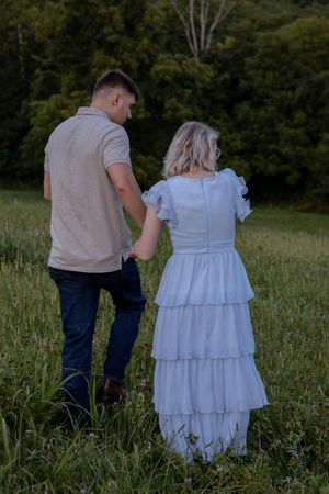 A couple walks hand in hand through a wildflower meadow at sunset.