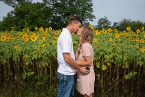 A couple shares a romantic moment in front of a sunflower field after getting engaged.