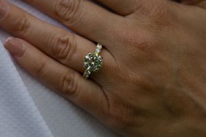 Close-up view of a sparkling diamond engagement ring on a hand against a blurred background.