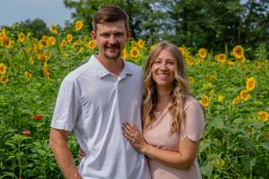 A couple poses together in a field of bright yellow sunflowers wearing coordinated outfits.