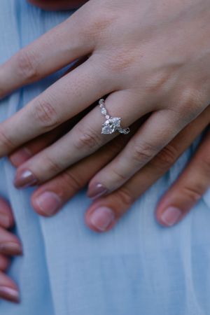 Close up shots of a diamond engagement ring on hand against light blue fabric.