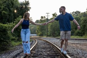 Multiple shots of a couple walking and posing along train tracks surrounded by trees.