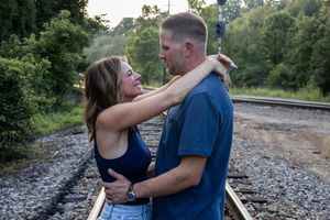 Couple in casual attire sharing tender moments on railway tracks during golden hour.