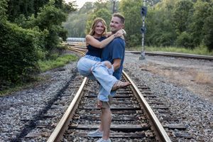 Playful couple posing together on rustic railroad tracks surrounded by greenery.