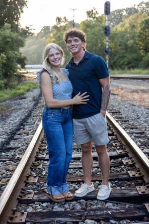 Couple in denim and navy outfits sharing candid moments on train tracks.