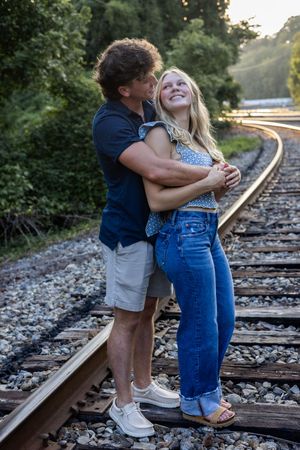 Romantic photoshoot featuring couple in casual wear on railroad tracks at dusk.