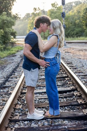 Couple in matching blue outfits sharing affectionate moments on railway tracks.