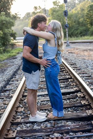 Casual couple's photography session on railroad tracks with natural backdrop.