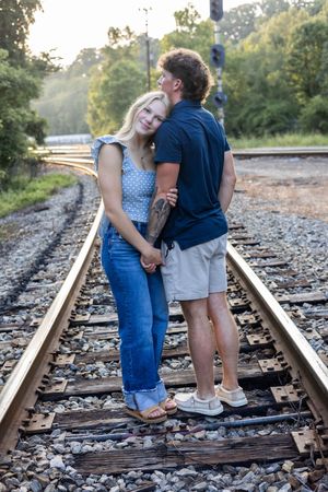 A romantic couple embraces on railroad tracks during a sunset photoshoot in a natural setting.
