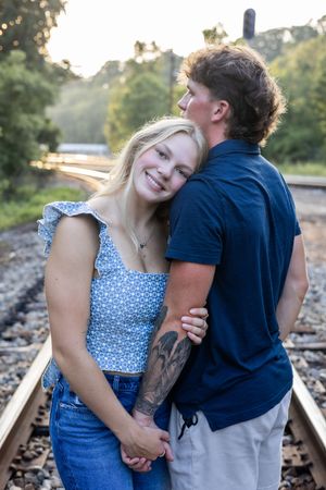 A couple shares an intimate moment while posing together on train tracks surrounded by greenery.