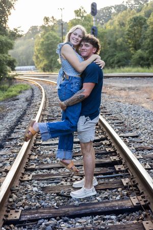 A playful couple embraces while balancing on railroad tracks during an outdoor photoshoot.