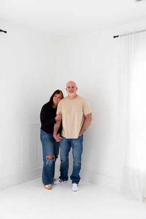 Two people stand together in a minimalist white room with ripped jeans and casual attire.