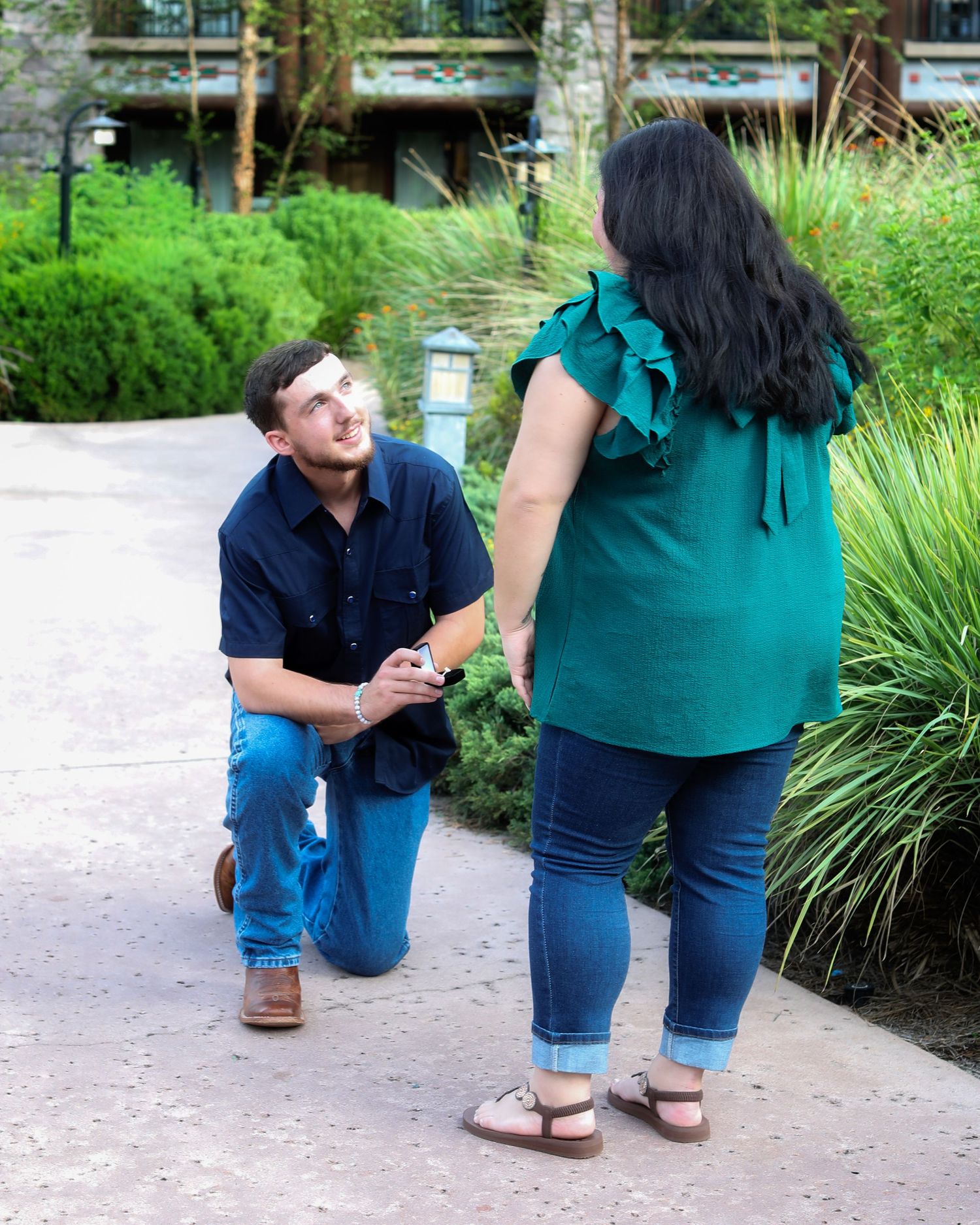 A candid moment shows a marriage proposal sequence taking place in a lush garden path with decorative grasses.