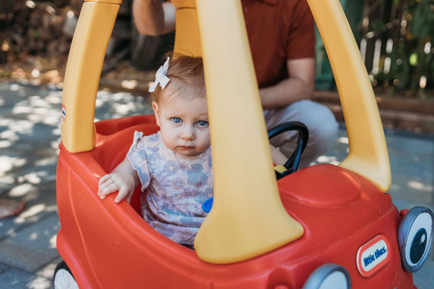 Five sequential photos showing a young child playing in a red and yellow Little Tikes Cozy Coupe toy car outdoors.