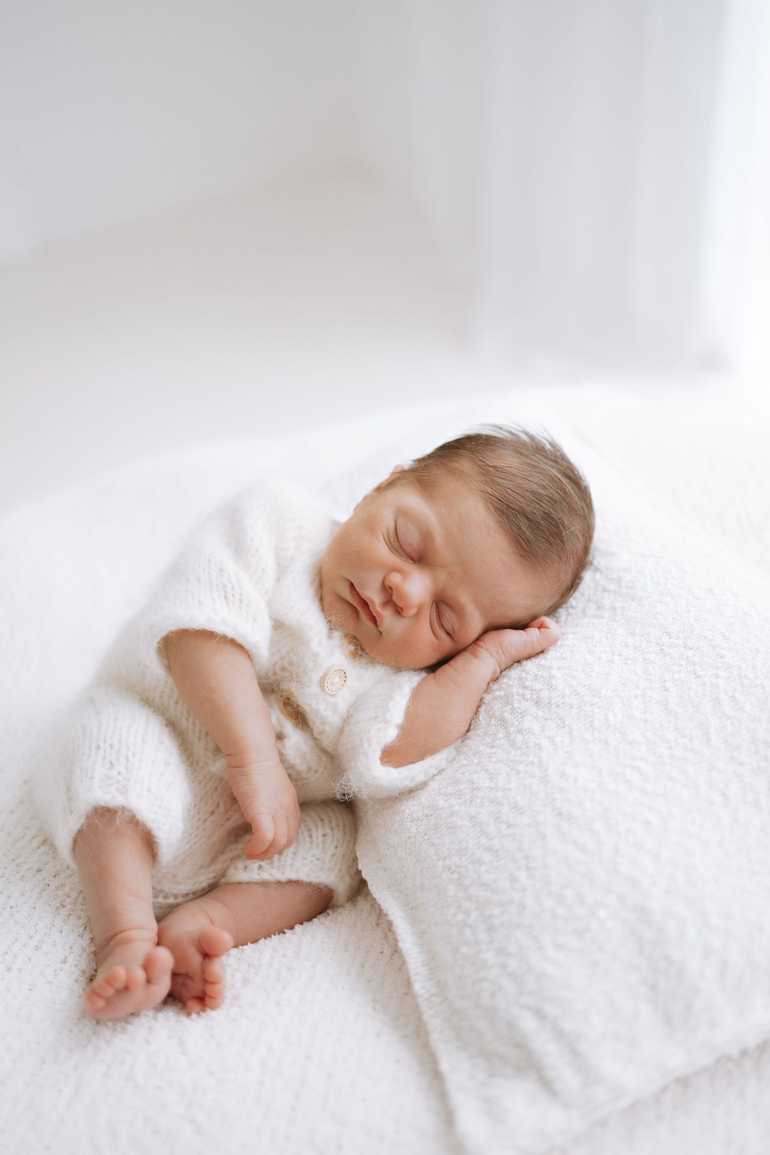 Sleeping newborn baby wrapped in soft white textured blanket lies peacefully on light background.