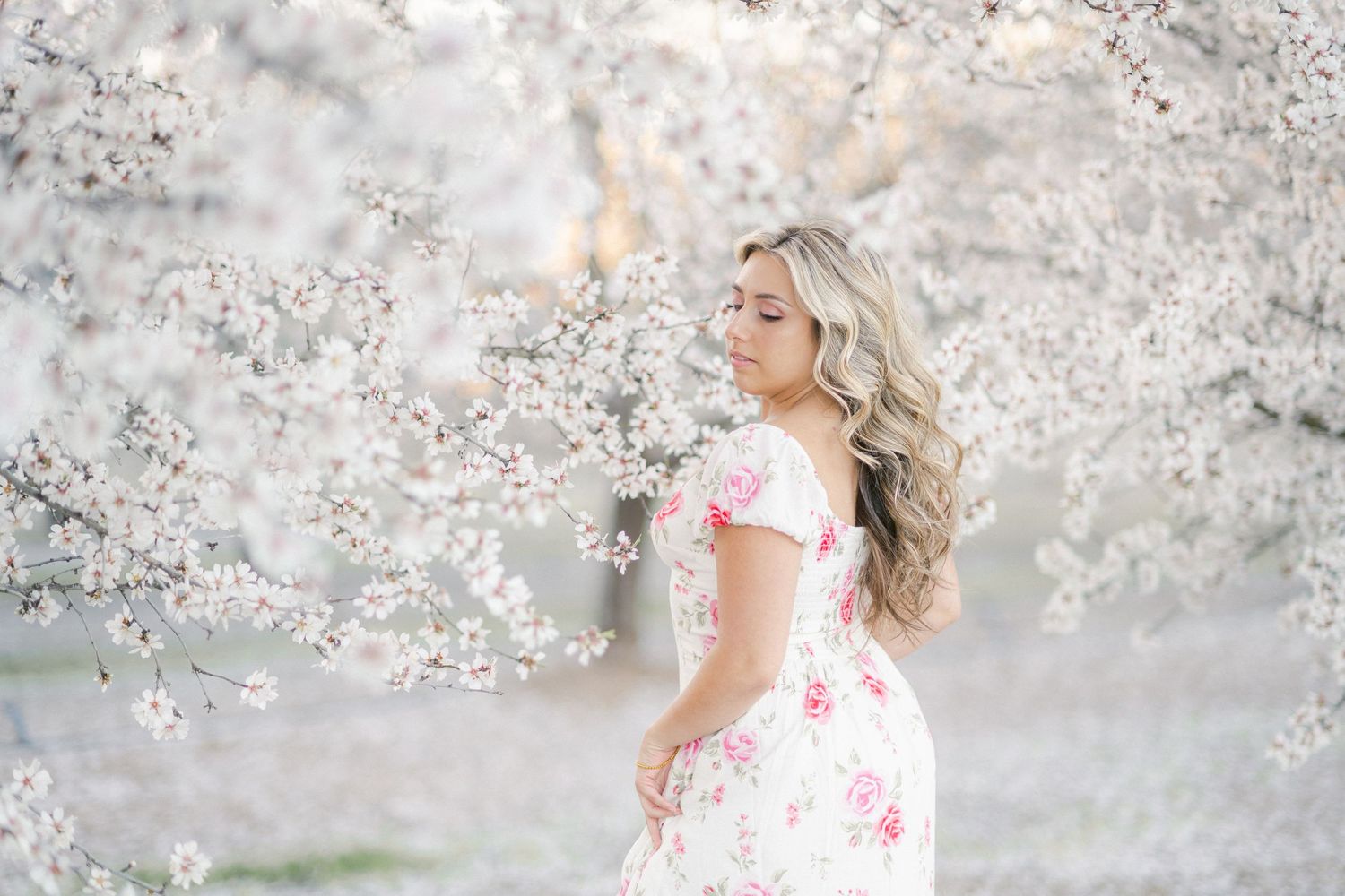 A flowy white and coral floral dress contrasts beautifully with delicate cherry blossoms blooming in the springtime.