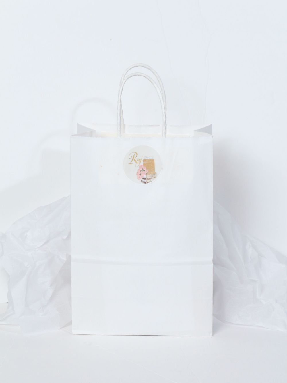 A simple white shopping bag with handles stands against a minimalist white background creating a clean retail look.